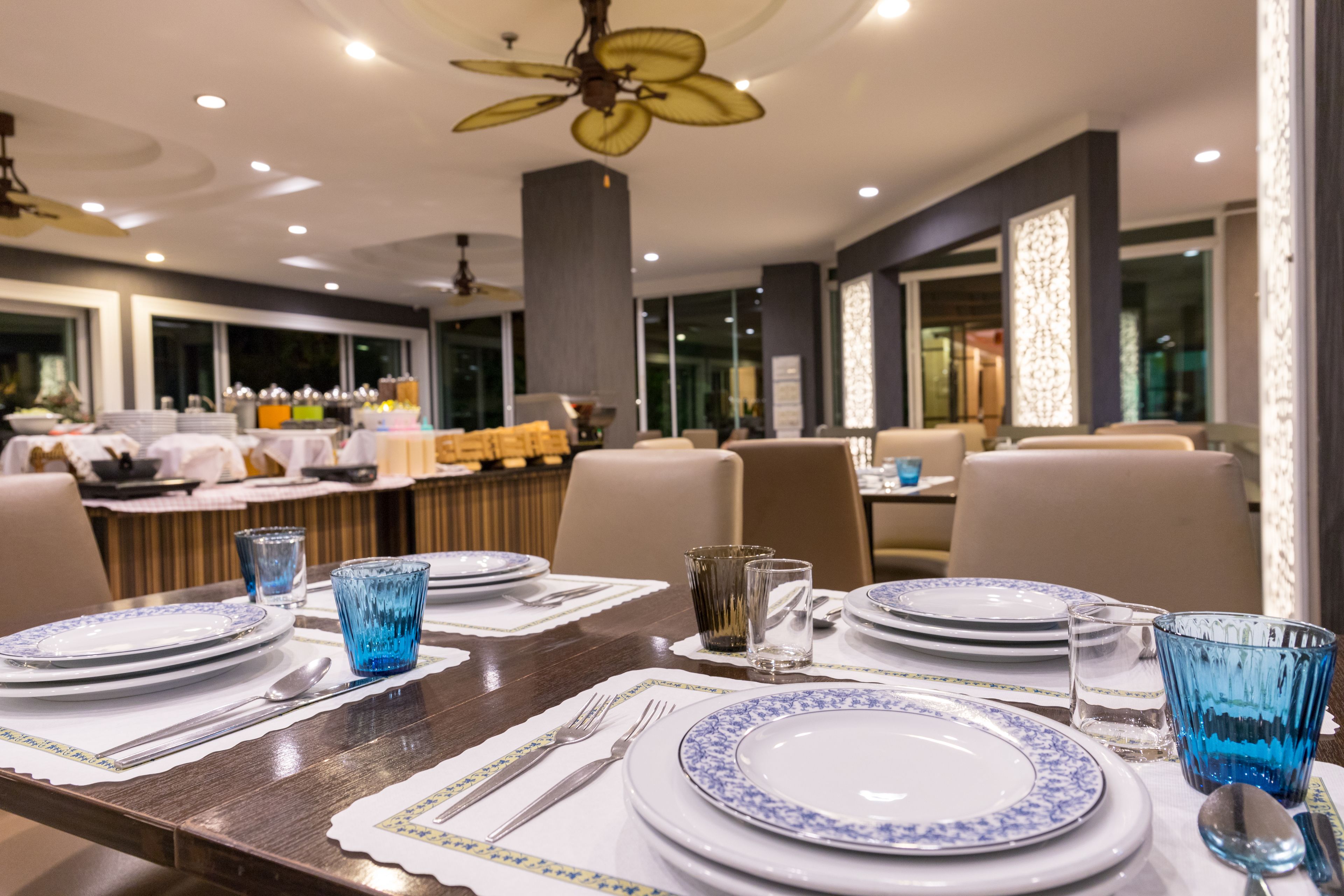 A dining area with tables set for a meal, featuring blue and white plates, silverware, and blue glassware.