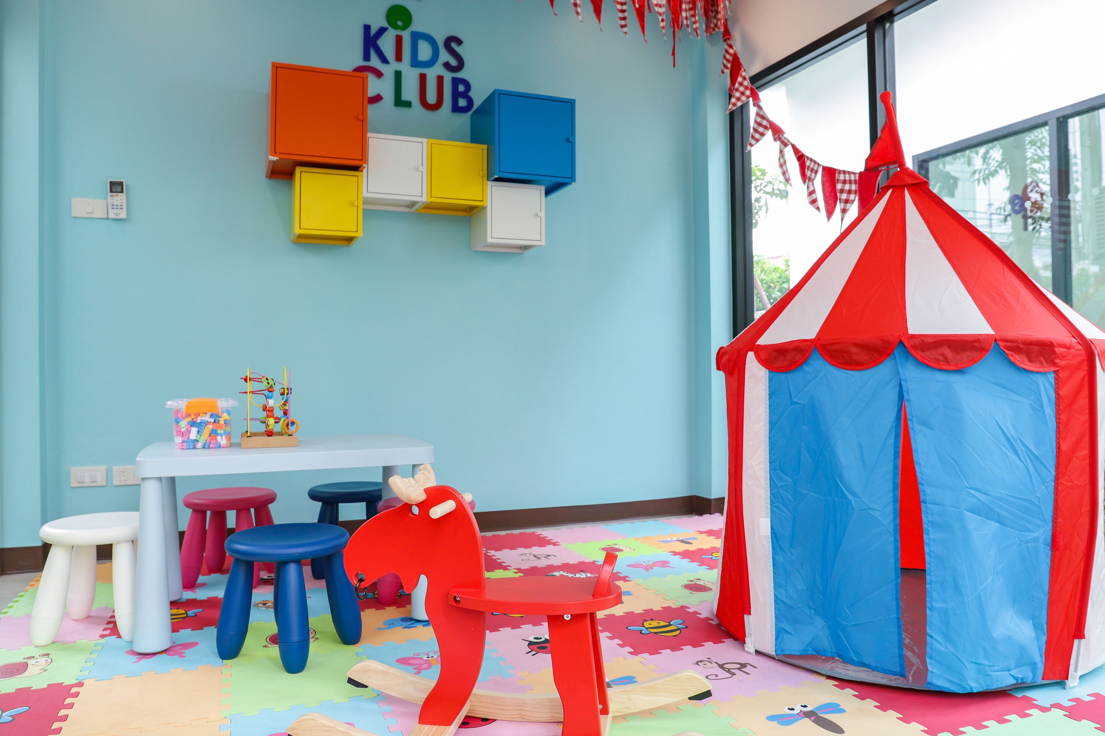 A children's playroom with colorful stools, a play table, and a tent.