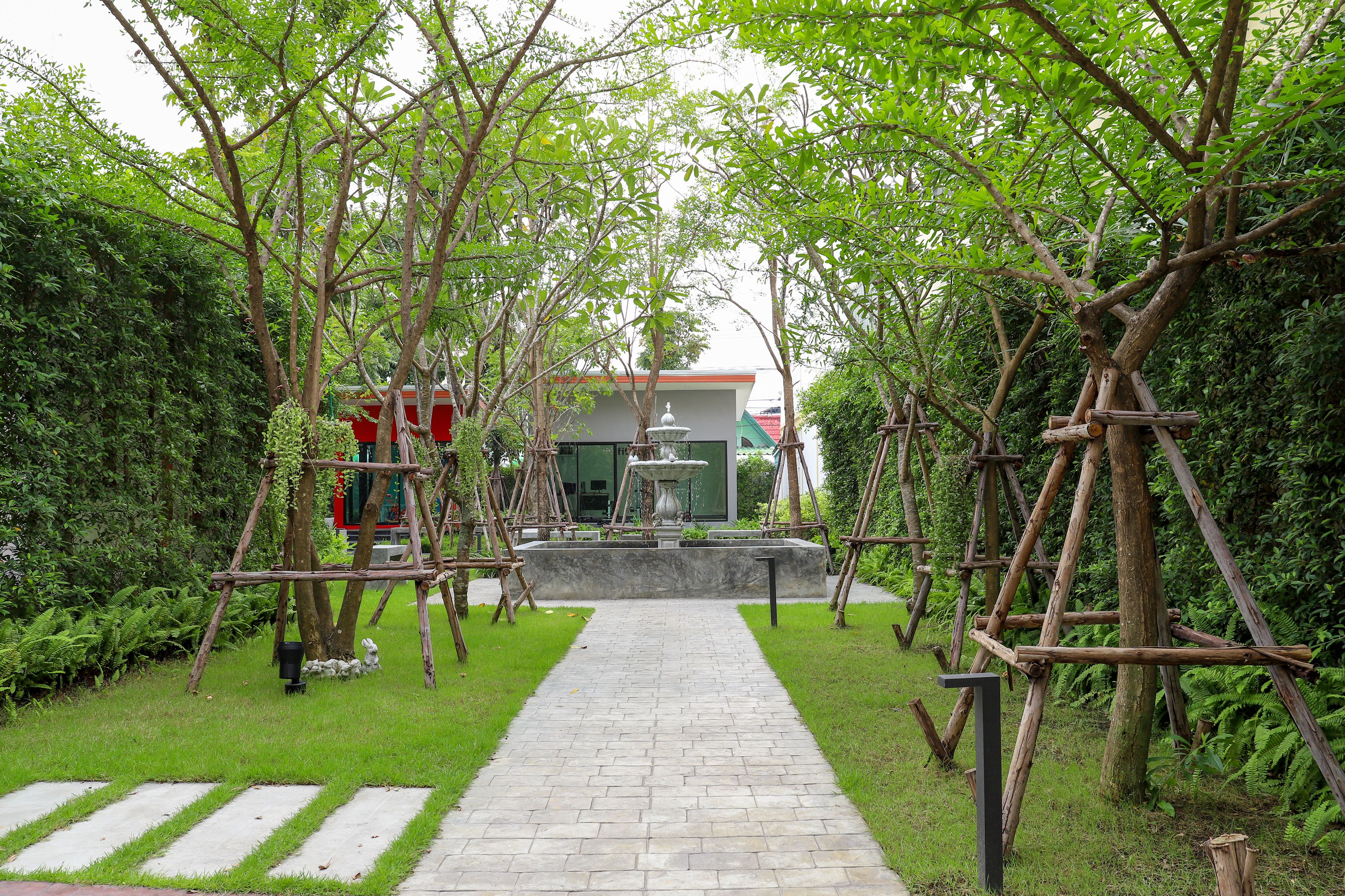 A pathway leading to a building with a fountain, surrounded by greenery and wooden structures.