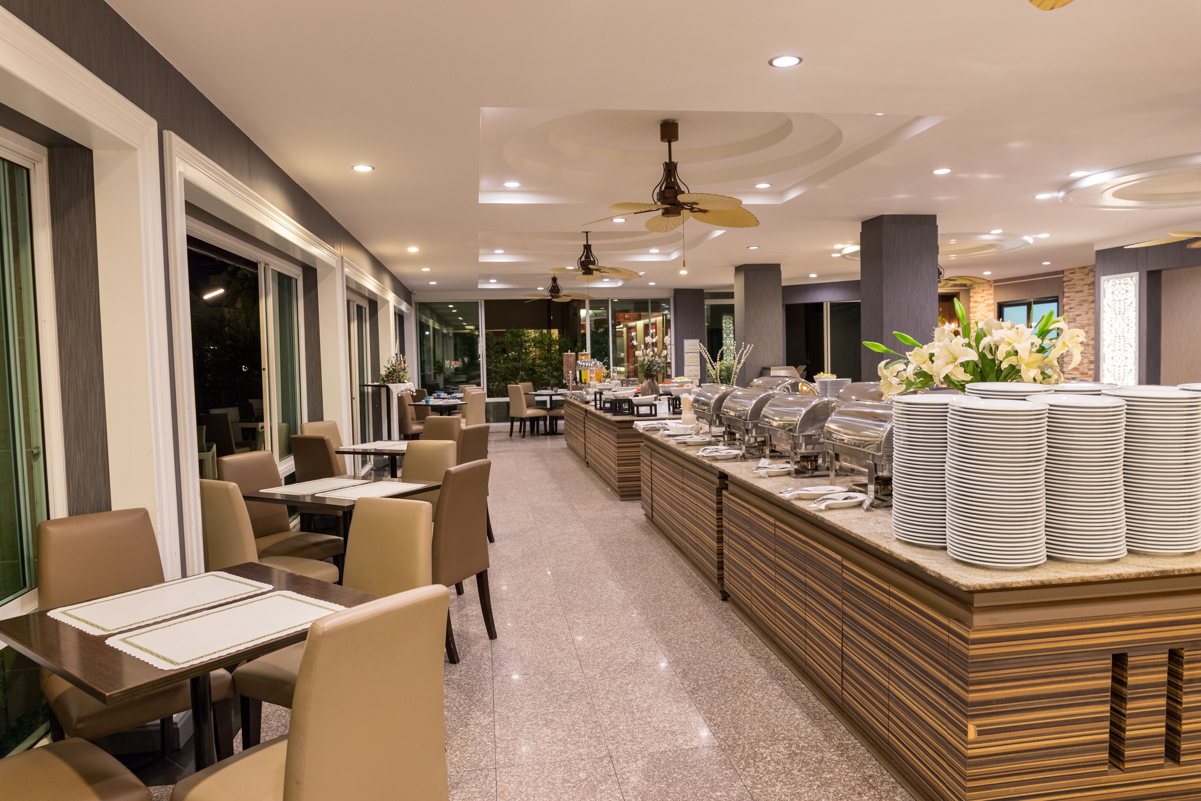 A modern restaurant with a long counter, multiple tables, and ceiling fans.