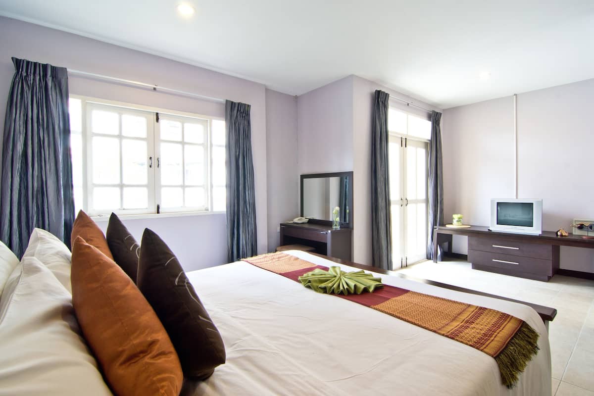 A hotel room with a large bed, a desk with a TV, and a window with curtains.