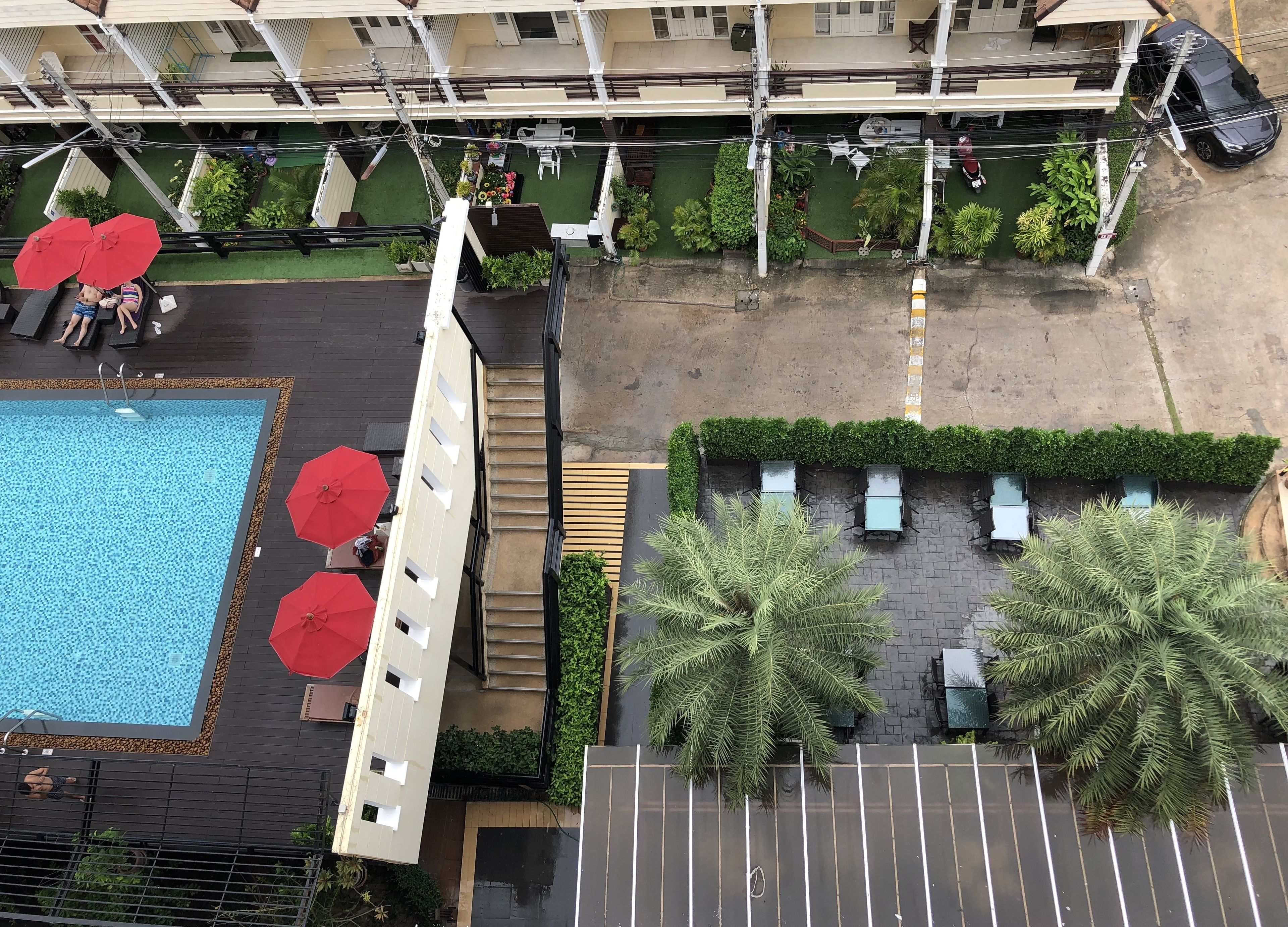 Un espace piscine aménagé sur le toit, avec une piscine, des parasols rouges et des chaises longues.