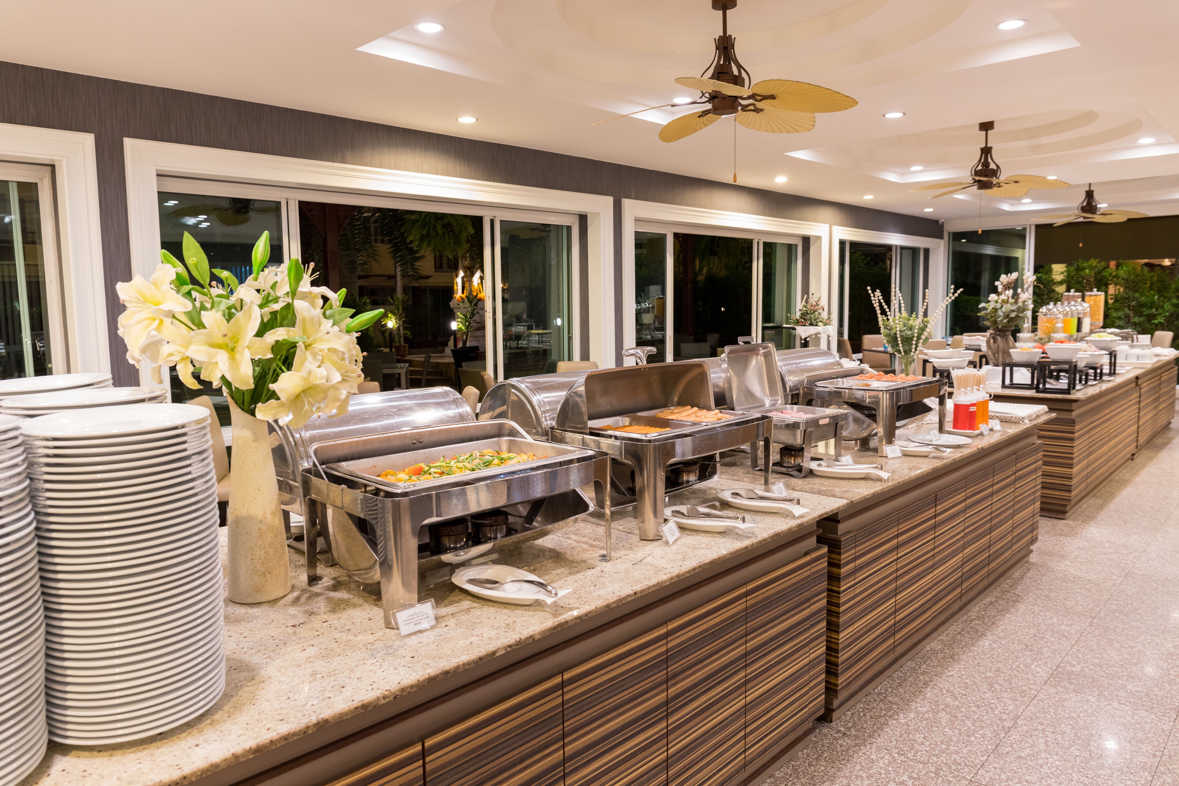 A buffet setup with multiple food stations, a large window with a view, and a ceiling fan.