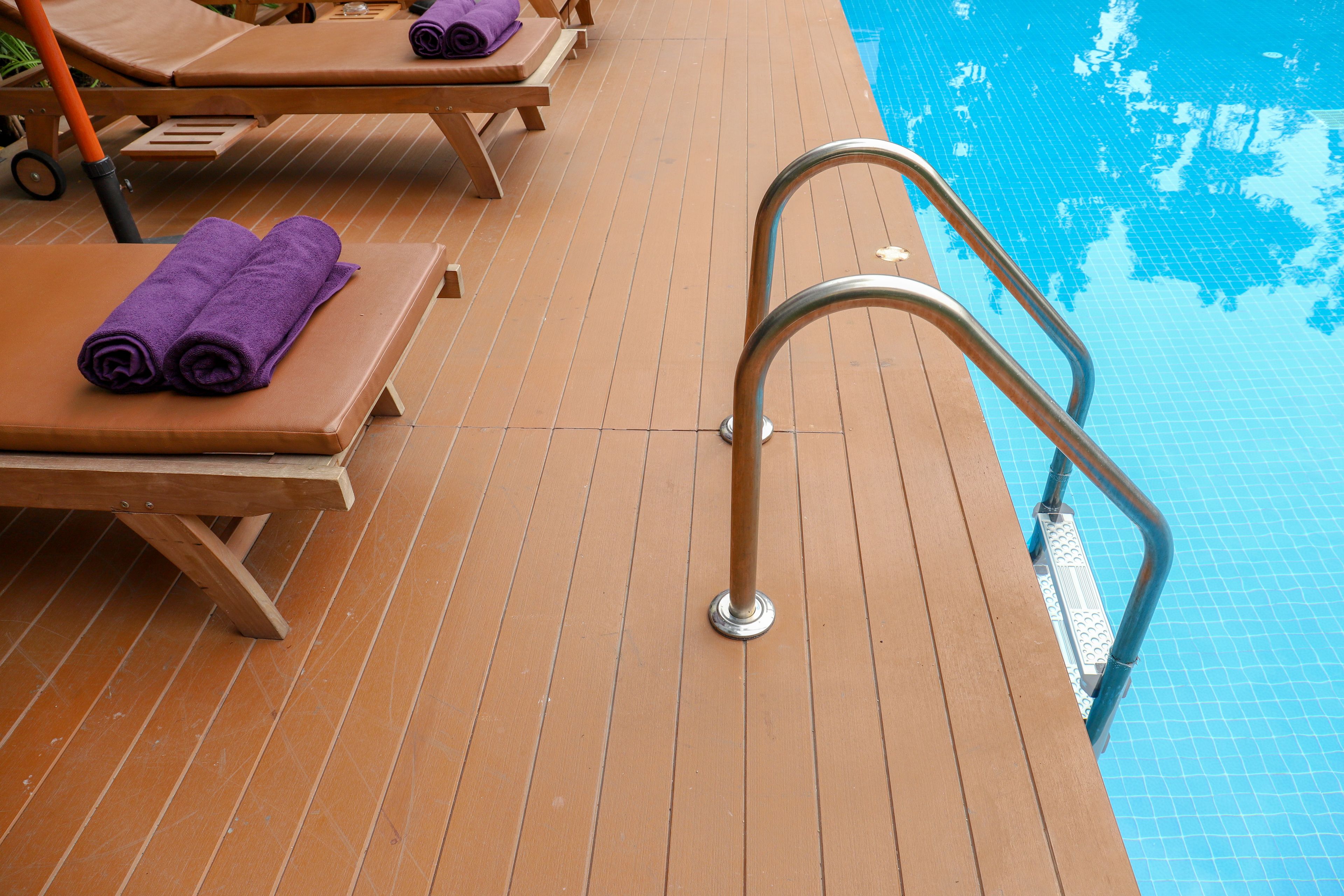 A poolside area with wooden loungers and a metal pool ladder.