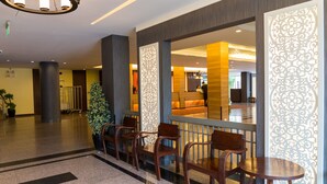 A lobby with a reception desk, wooden chairs, a potted plant, and decorative panels.