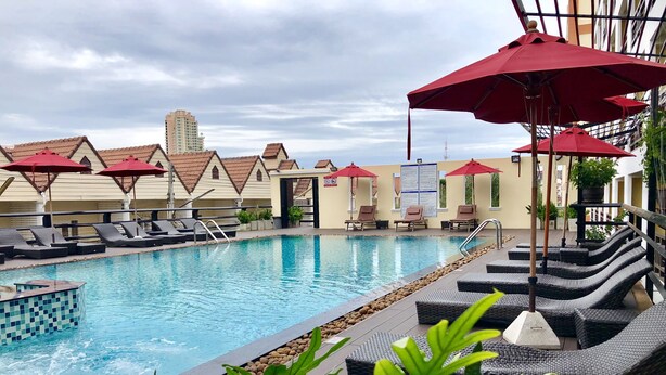 A swimming pool with lounge chairs and red umbrellas, surrounded by buildings with tiled roofs.