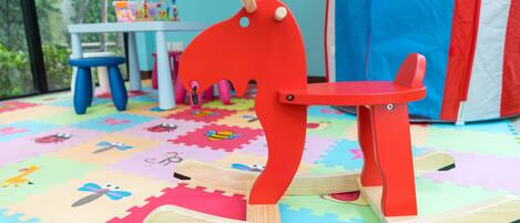A rocking horse on a colorful play mat with a table and chairs in the background.