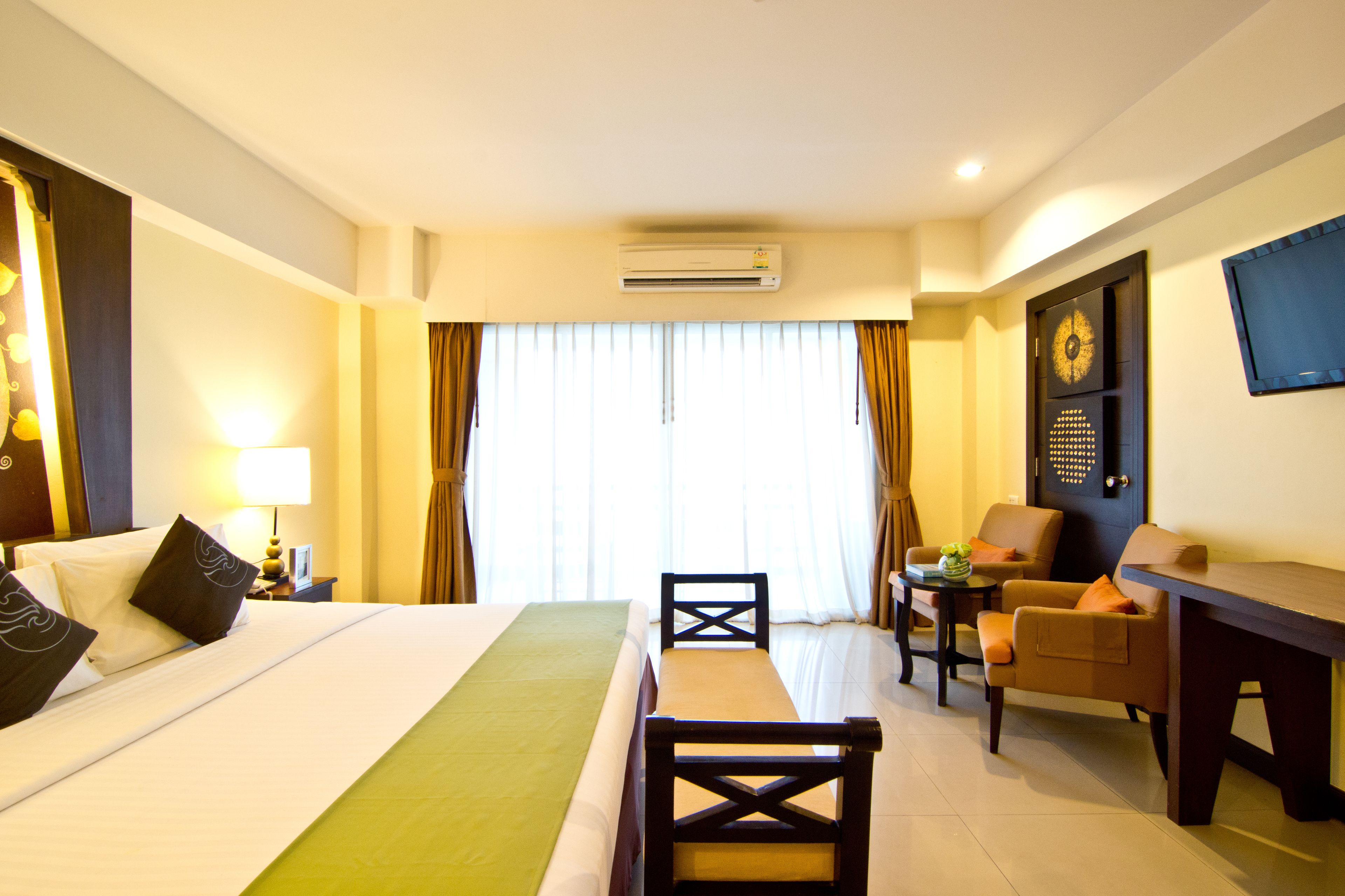 A hotel room with a bed, a desk, a chair, a television, and an air conditioning unit.
