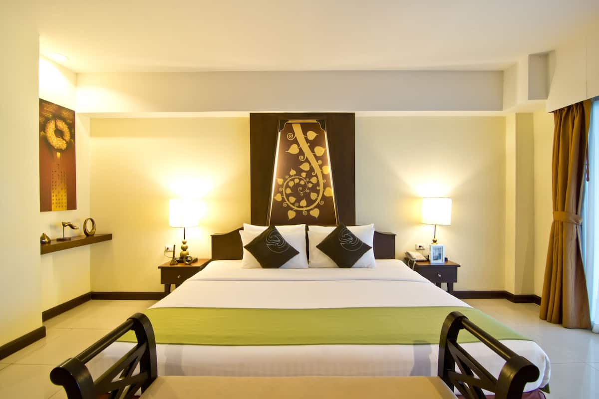 A hotel room with a large bed, two bedside tables, a headboard with a decorative panel, and a green throw on the bed.