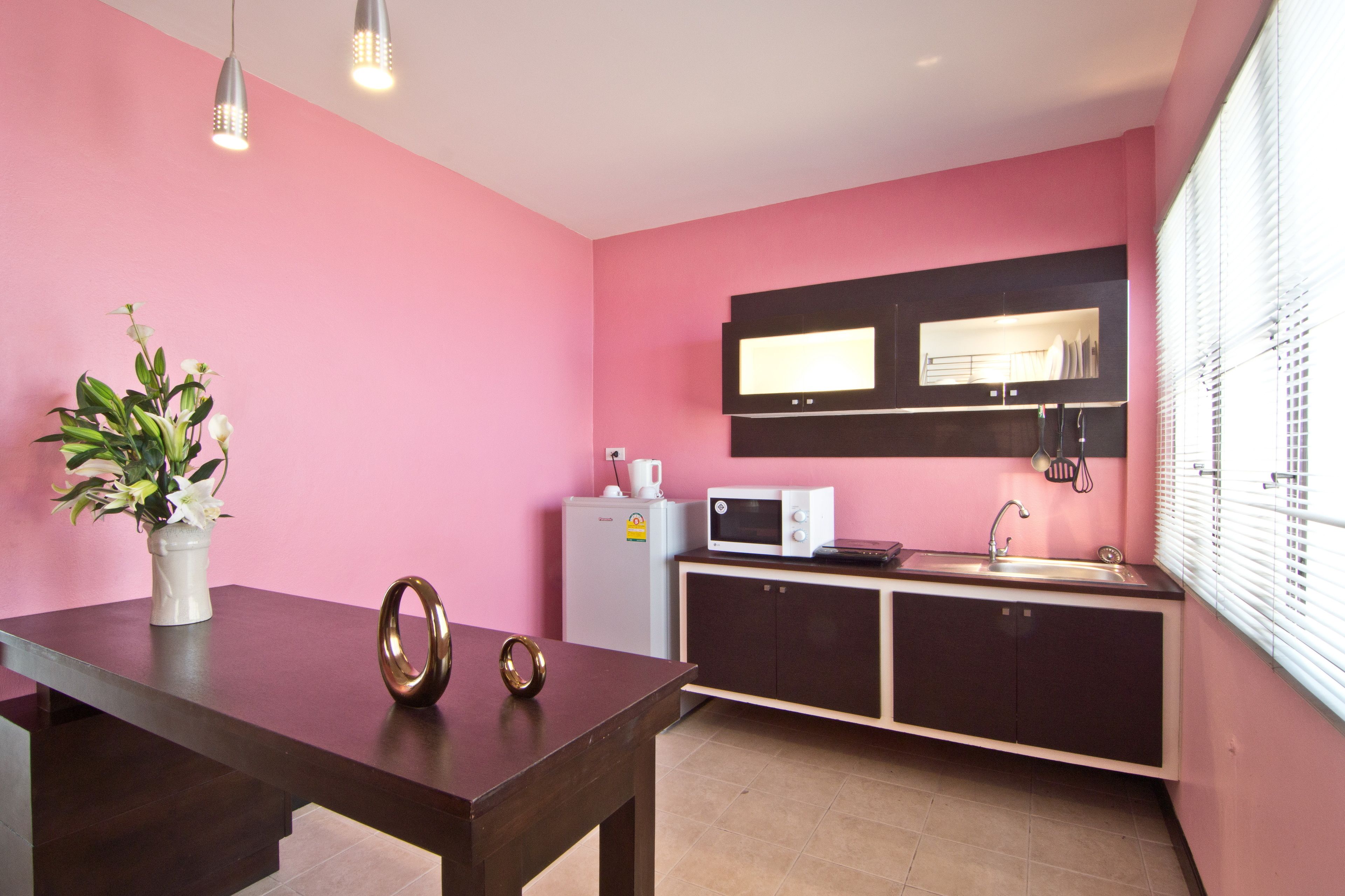 Een keuken met roze muren, een magnetron, een koelkast, een spoelbak en een bloevas op de tafel.
