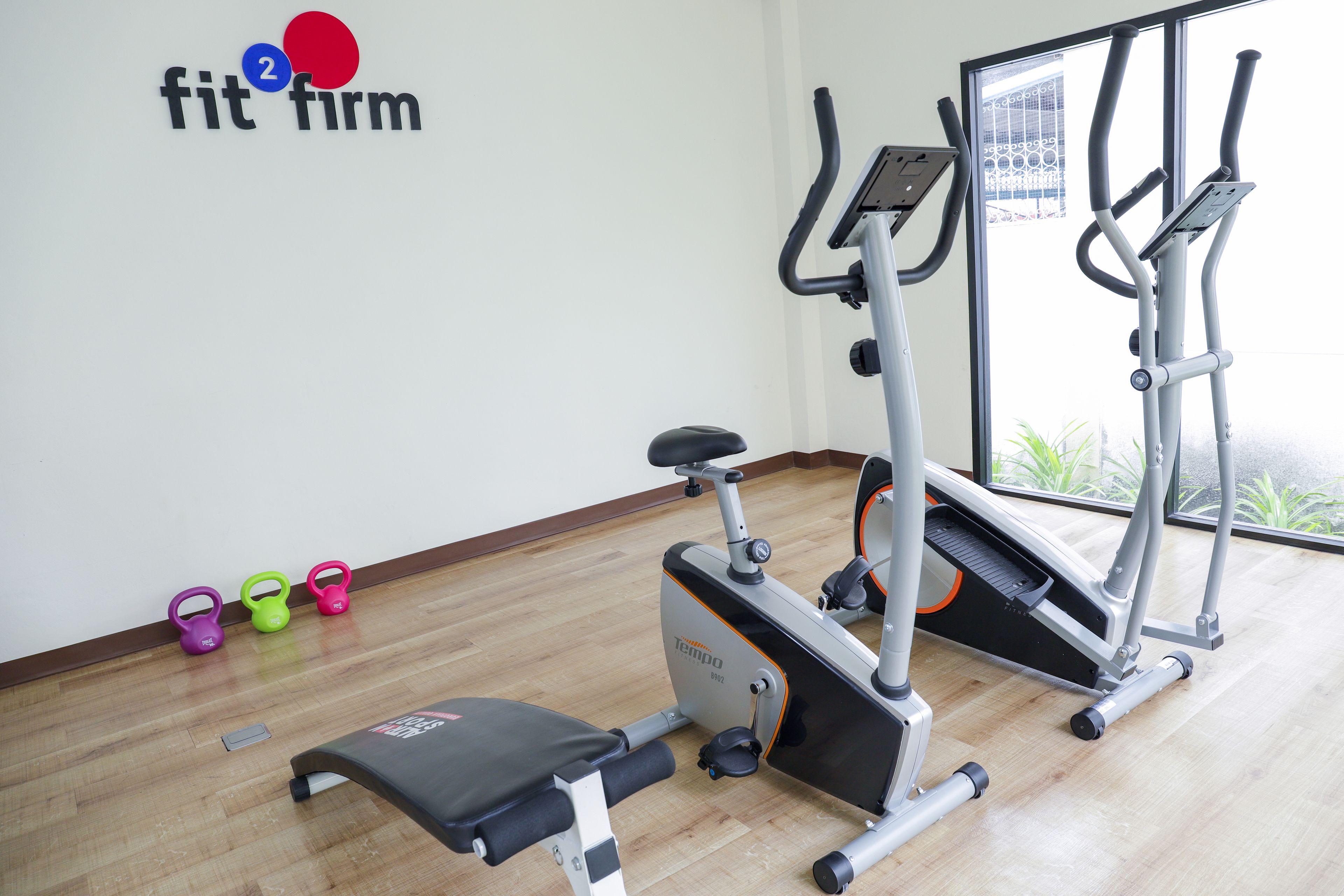 A fitness room with an elliptical machine, a bench, and kettlebells.