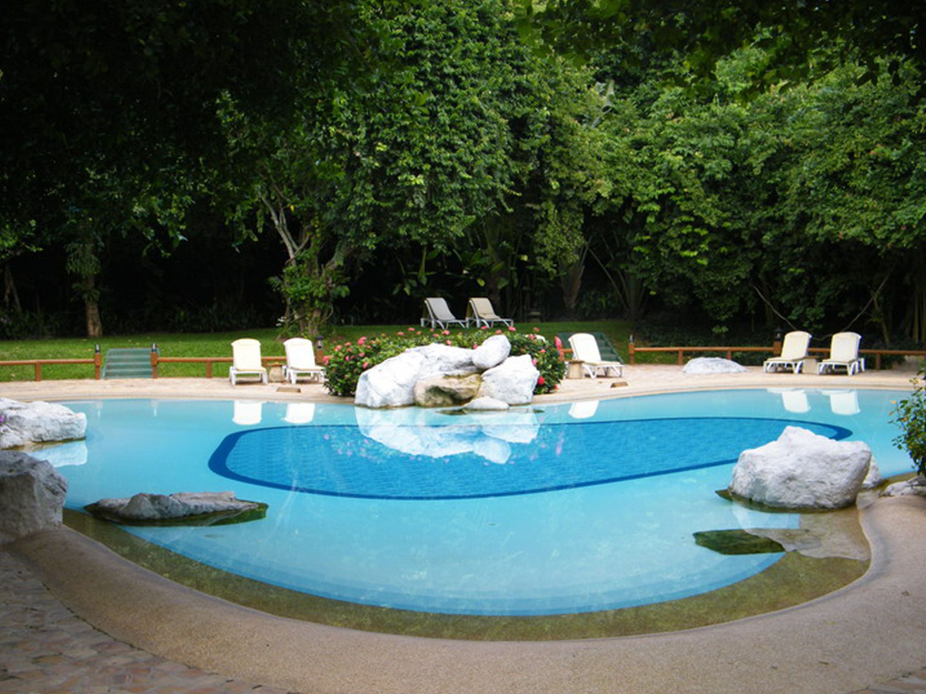 Una piscina con sillas de descanso blancas y grandes rocas.
