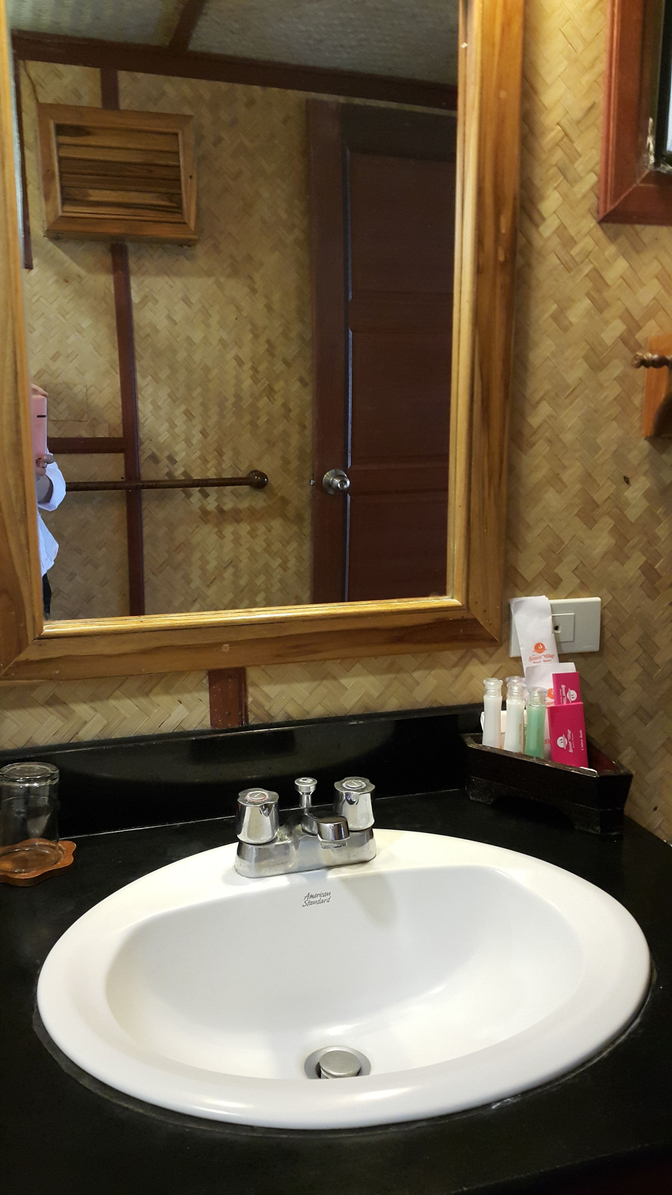Une salle de bain avec un miroir encadré en bois, un lavabo blanc avec un seul robinet et des articles de toilette posés sur le comptoir.