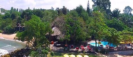 A beachside resort with a pool, lounge chairs, and a thatched-roof structure.