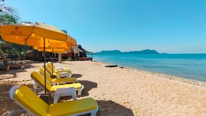 Une plage avec des chaises longues et des parasols jaunes, un rivage sablonneux et une mer calme.