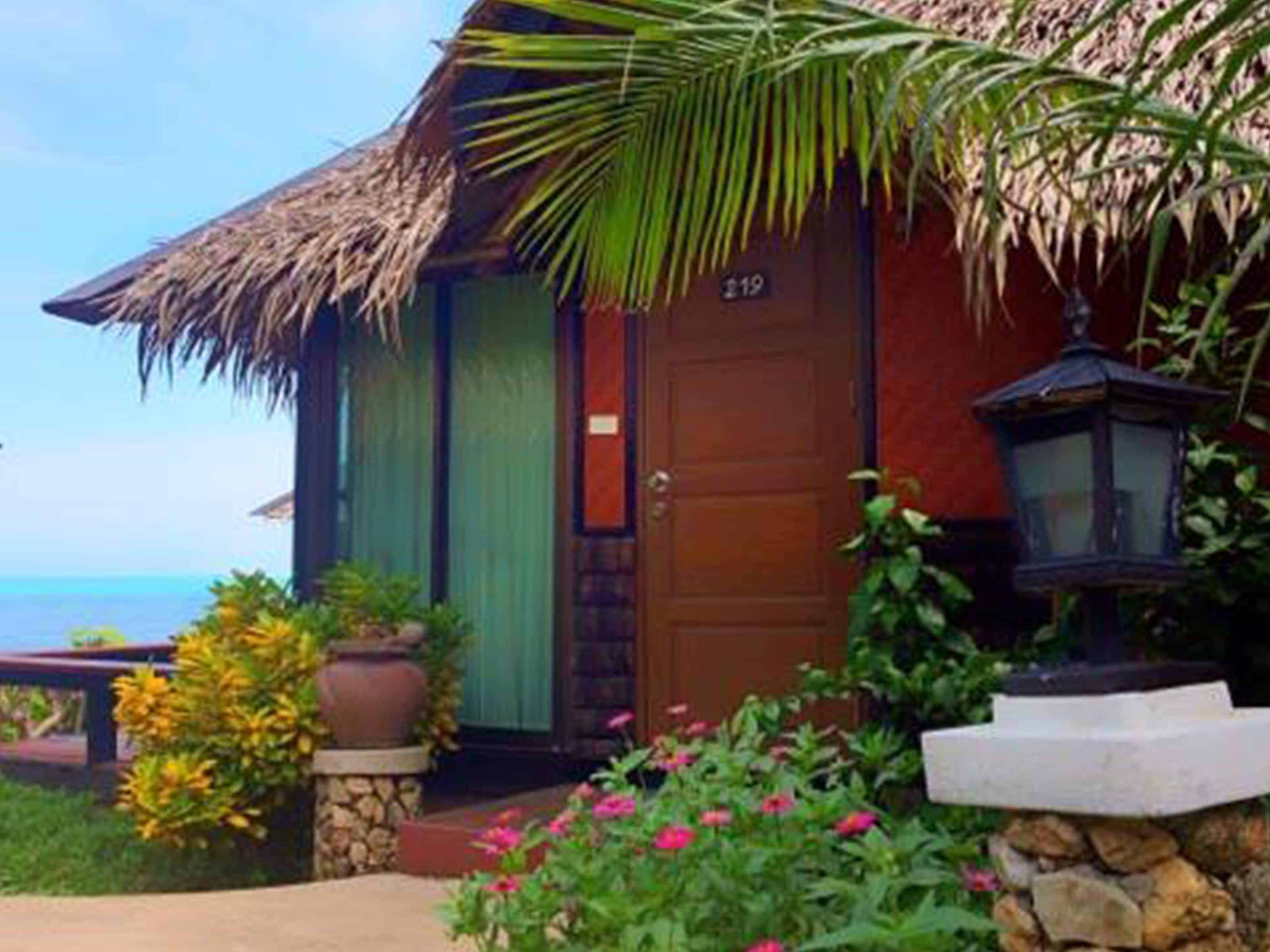 A tropical-style building with a thatched roof, a wooden door, and a stone pathway leading to the entrance.