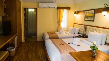 Habitación de hotel con dos camas, un escritorio de madera, un televisor y un ventilador de techo.