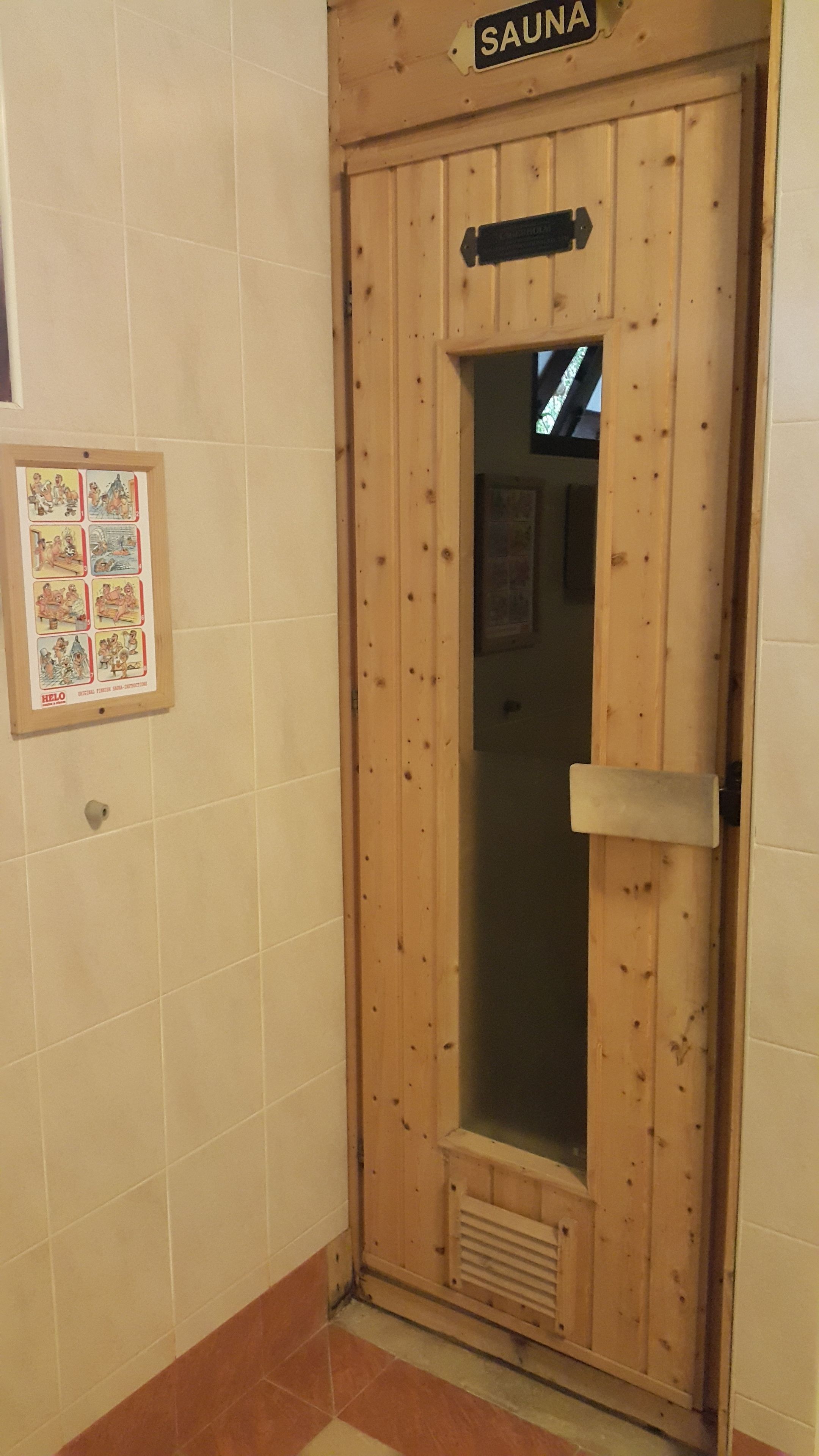 A wooden door labeled "SAUNA" with a small window and a ventilation grille at the bottom.
