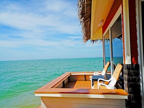 A wooden boat with a thatched roof, white plastic chairs, and a view of the ocean. - Sunset Village Beach Resort (Sattahip)