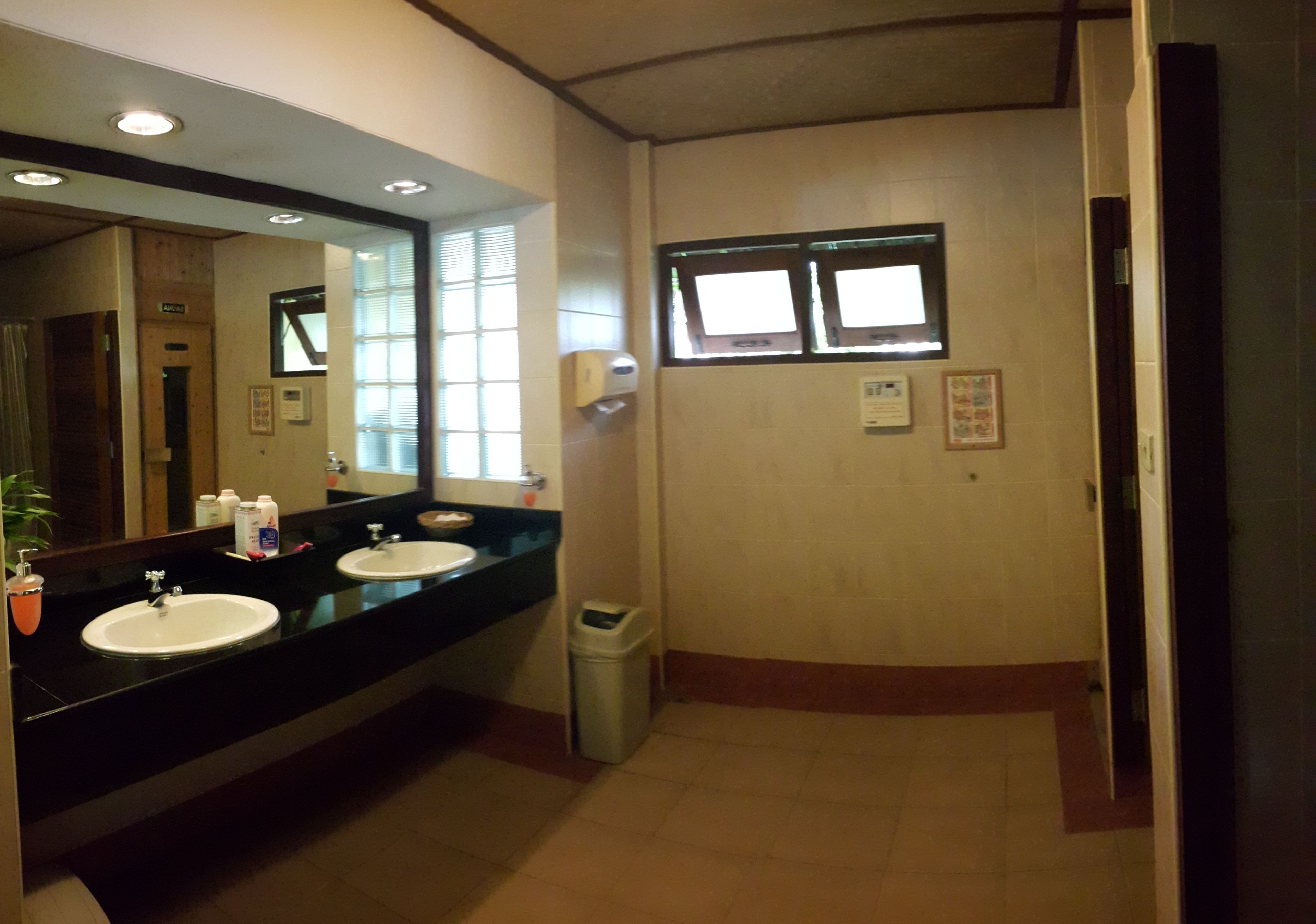 A bathroom with two sinks, a mirror, a trash bin, and a window.