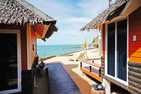 Una casa de playa de madera con techo de paja, una terraza de madera y vista al océano.