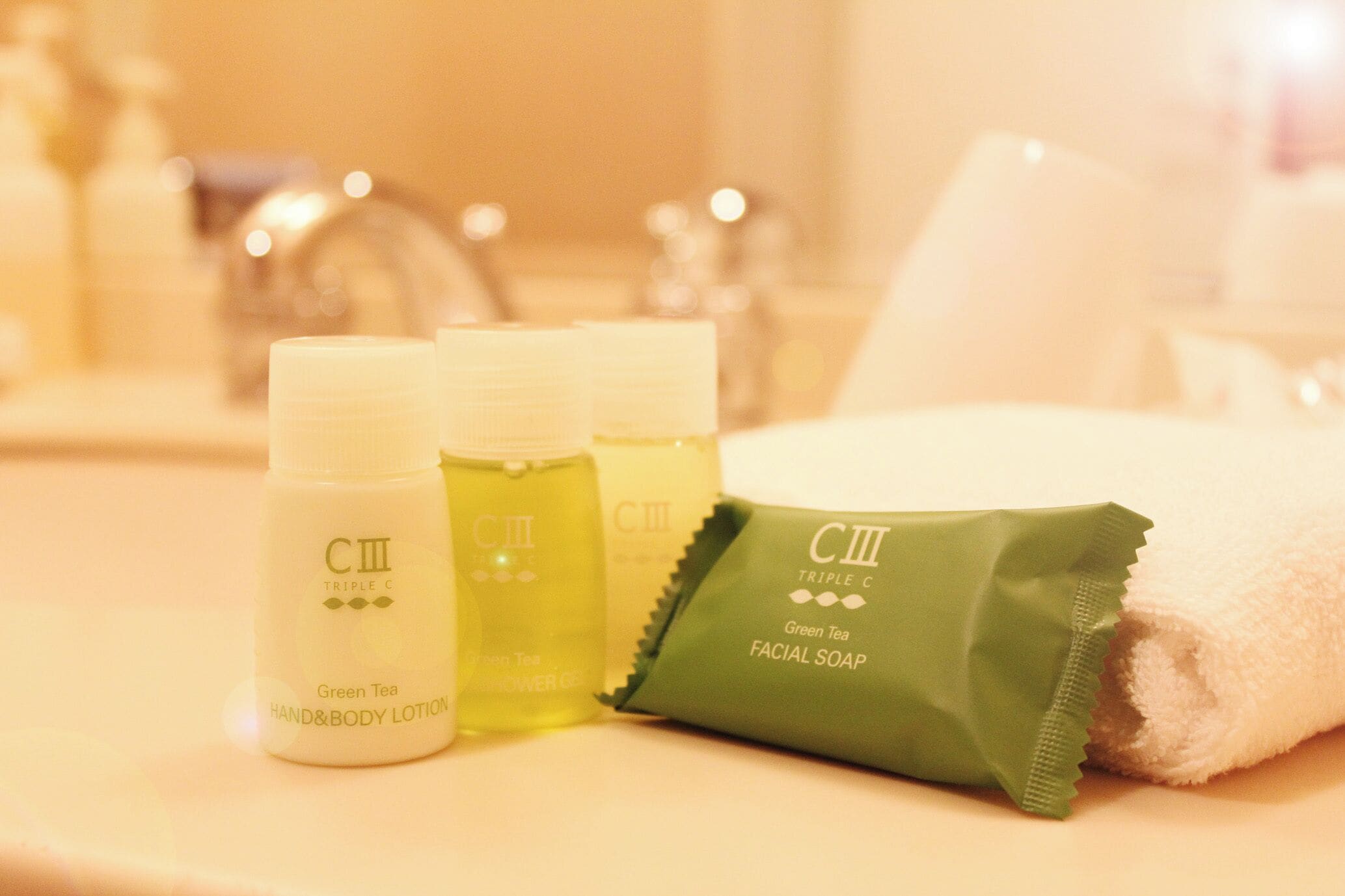 A bathroom sink with three bottles of green tea hand and body lotion and a green facial soap bar.