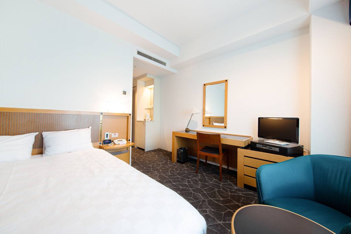Ein Hotelzimmer mit einem Bett, einem Schreibtisch mit Computer, einem Fernseher und einem Sessel.
