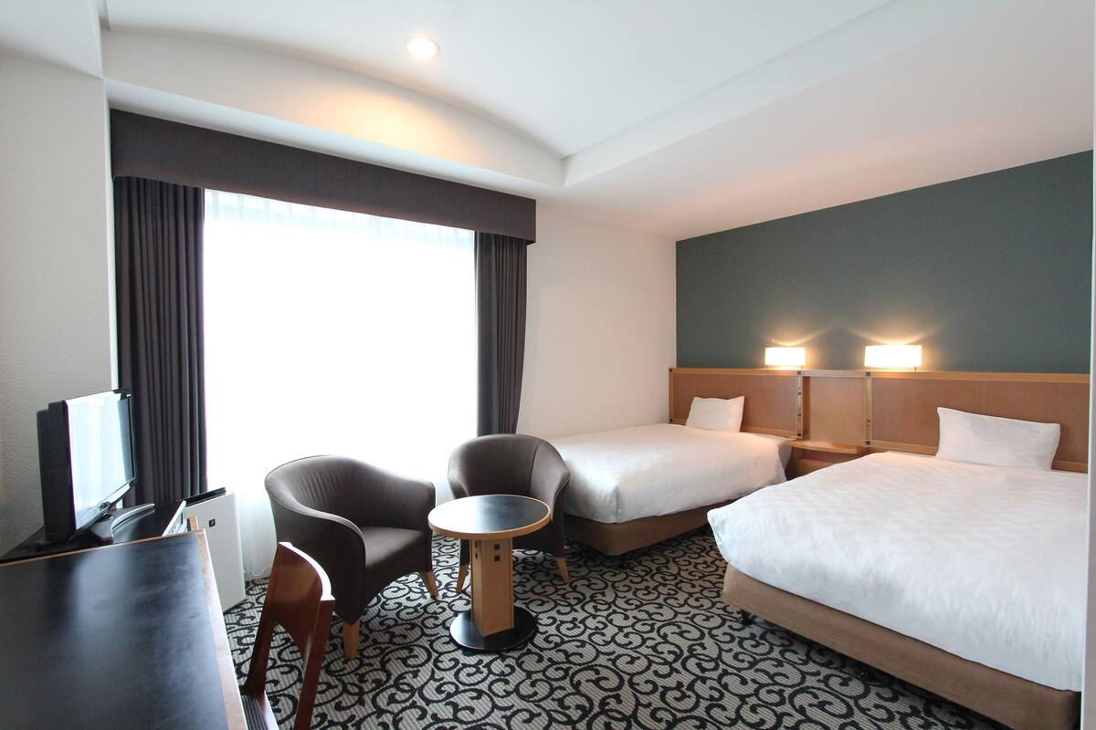 Ein Hotelzimmer mit Bett, zwei Nachttischen, einem Schreibtisch, einem Sessel und einem Fernseher.