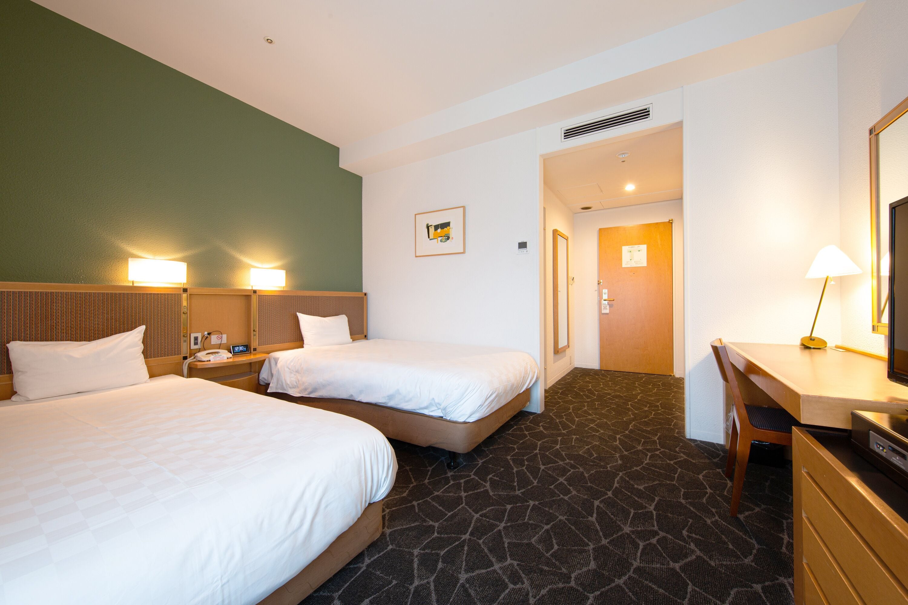 A hotel room with two beds, a desk, a chair, a lamp, and a picture on the wall.