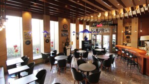 Un restaurante con varias mesas y sillas, una zona de bar y amplios ventanales con flores.