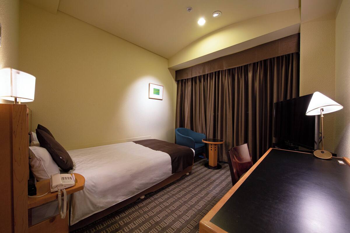 Ein Hotelzimmer mit Bett, Schreibtisch, Stuhl, Fernseher und Telefon.