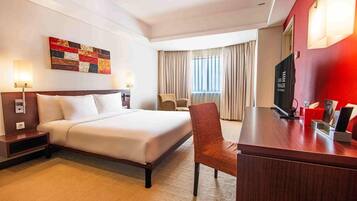 Ein Hotelzimmer mit Bett, Schreibtisch, Stuhl, Fernseher und einem Bild an der Wand.
