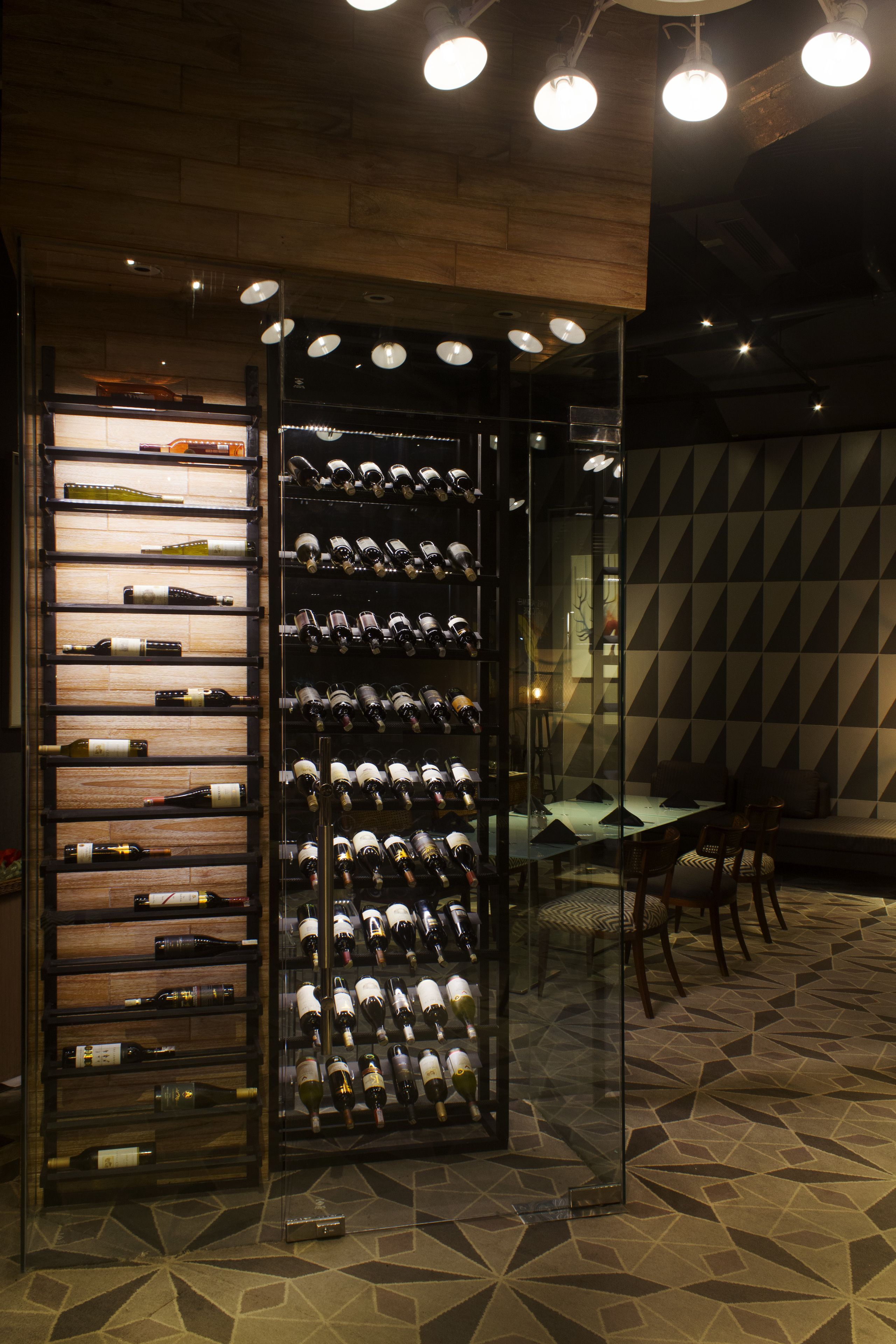 A wine cellar with shelves of wine bottles, a glass display case, and a dining area with chairs and a table.