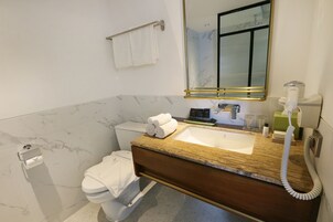 Un baño con pared de baldosas de mármol, tocador de madera con lavamanos, inodoro y espejo con marco dorado.