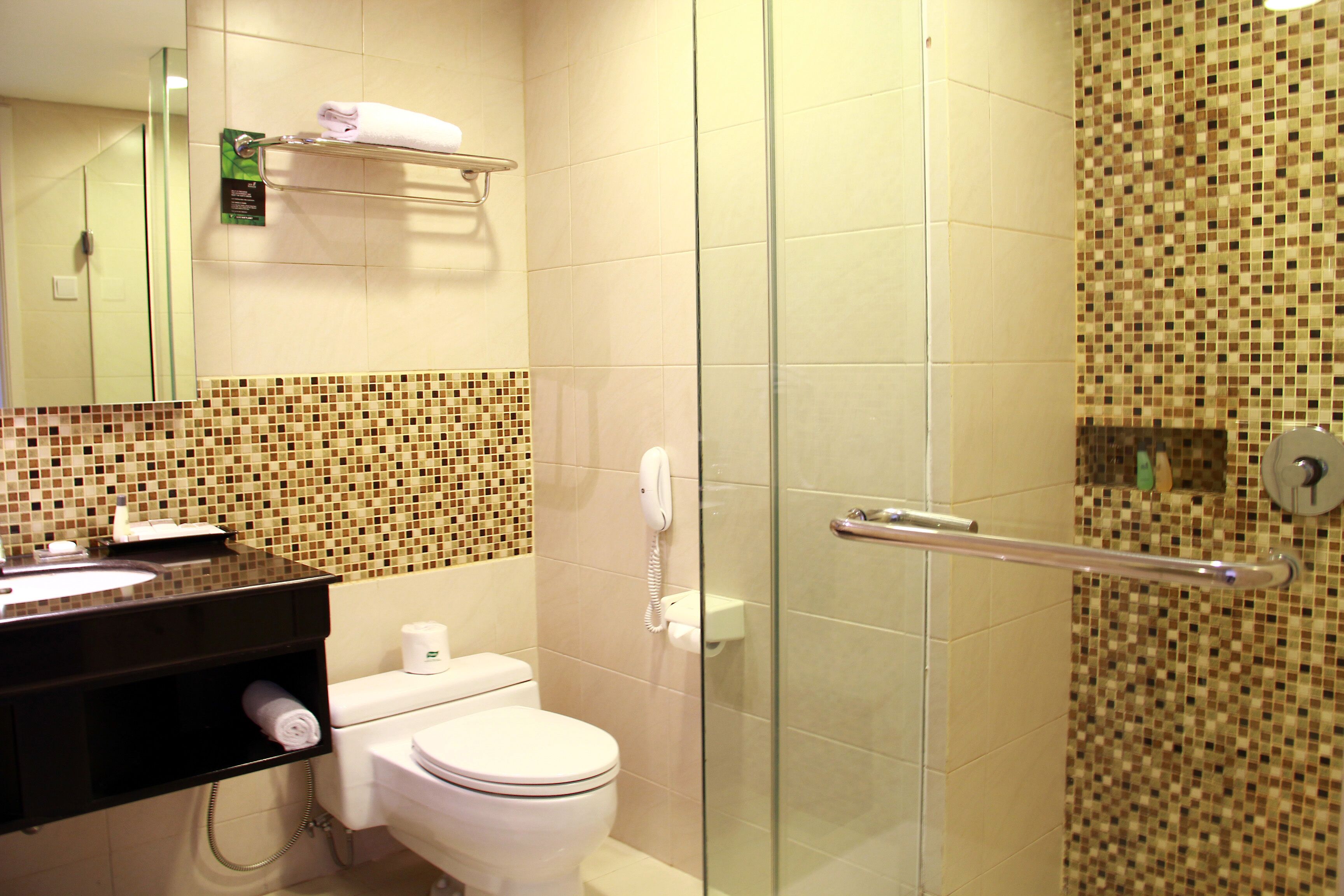 Un baño con inodoro, lavamanos, cabina de ducha de vidrio, toallero y teléfono.