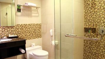 Un baño con inodoro, lavamanos, cabina de ducha de vidrio, toallero y teléfono.
