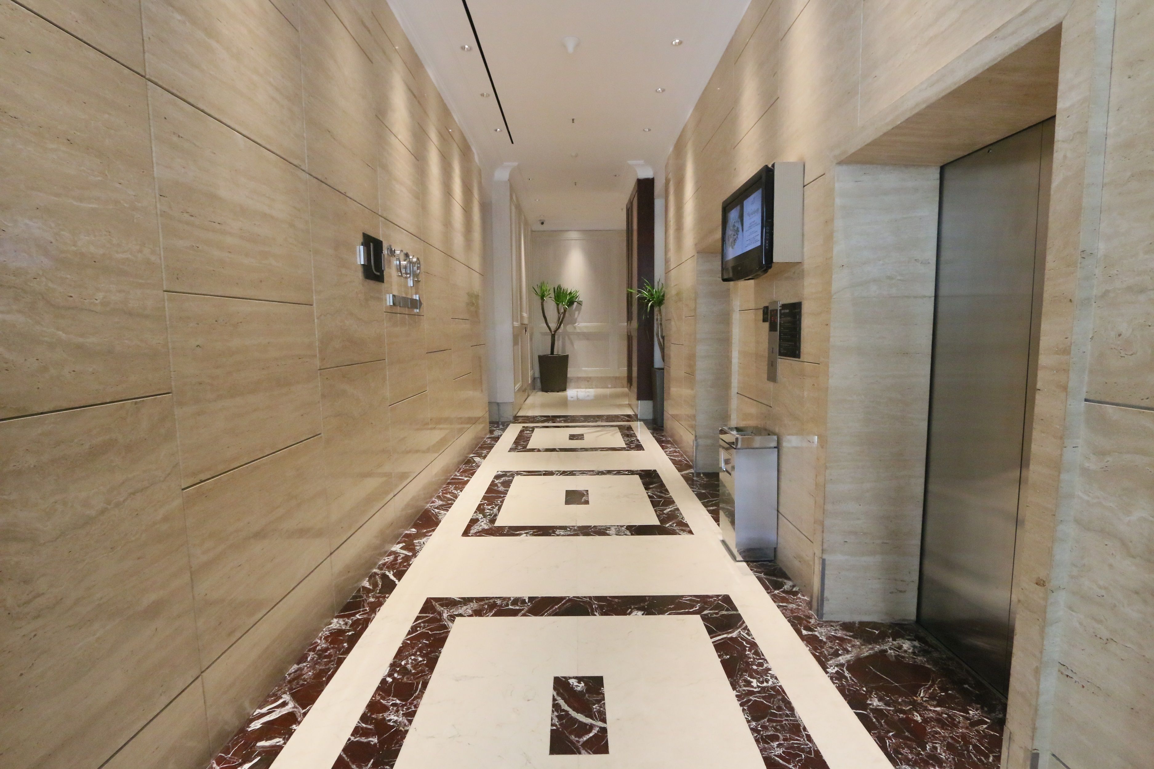 A modern hallway with marble flooring, a potted plant, and a television mounted on the wall.