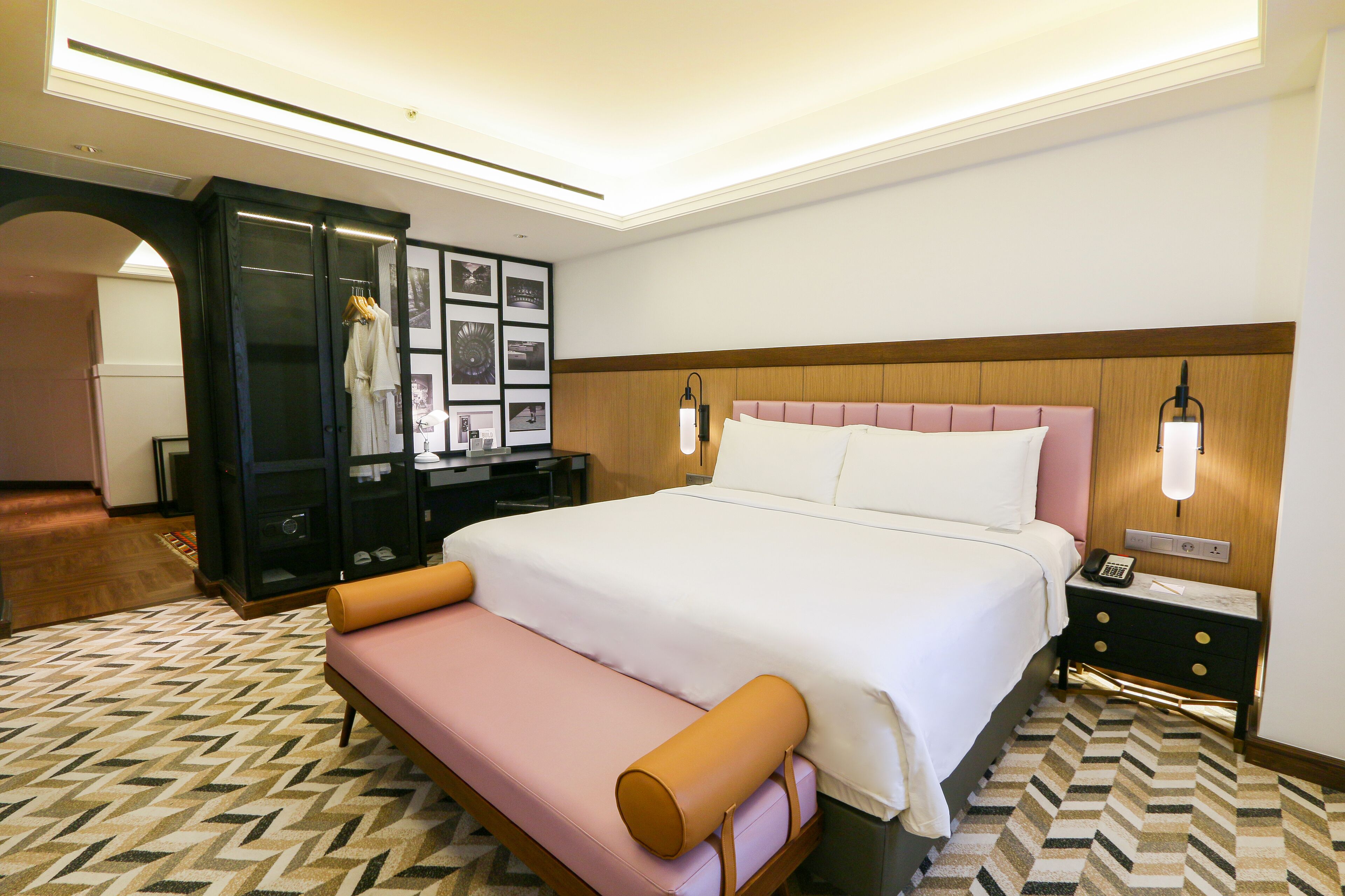 A hotel room with a large bed, a bench, a nightstand, and a wardrobe.