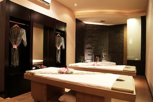 A spa room with two massage tables, dark wood cabinets, and a stone wall.