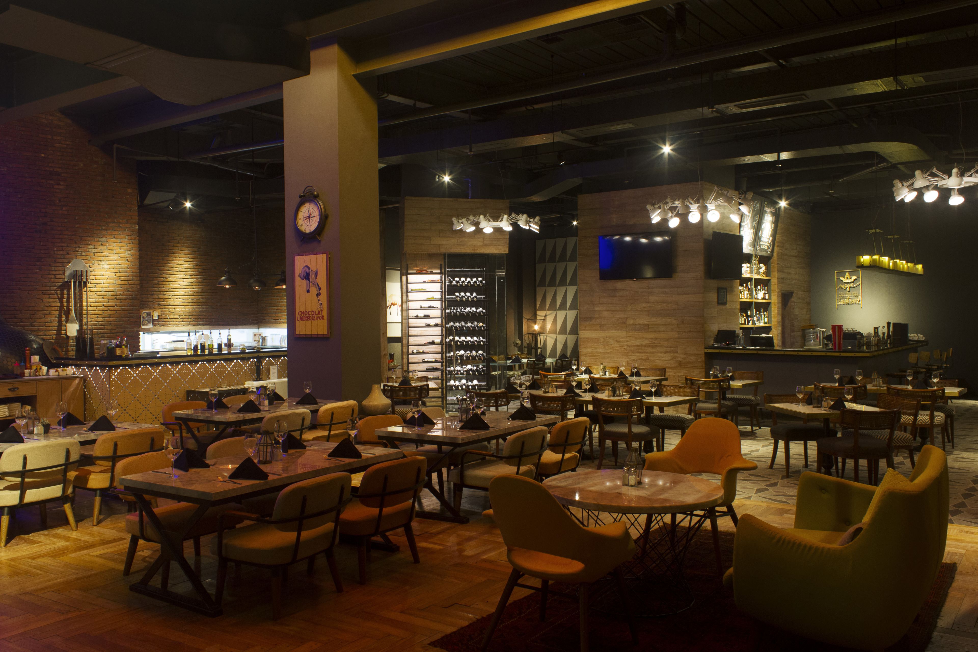 A restaurant with multiple dining tables and chairs, a bar area, and a wine display.