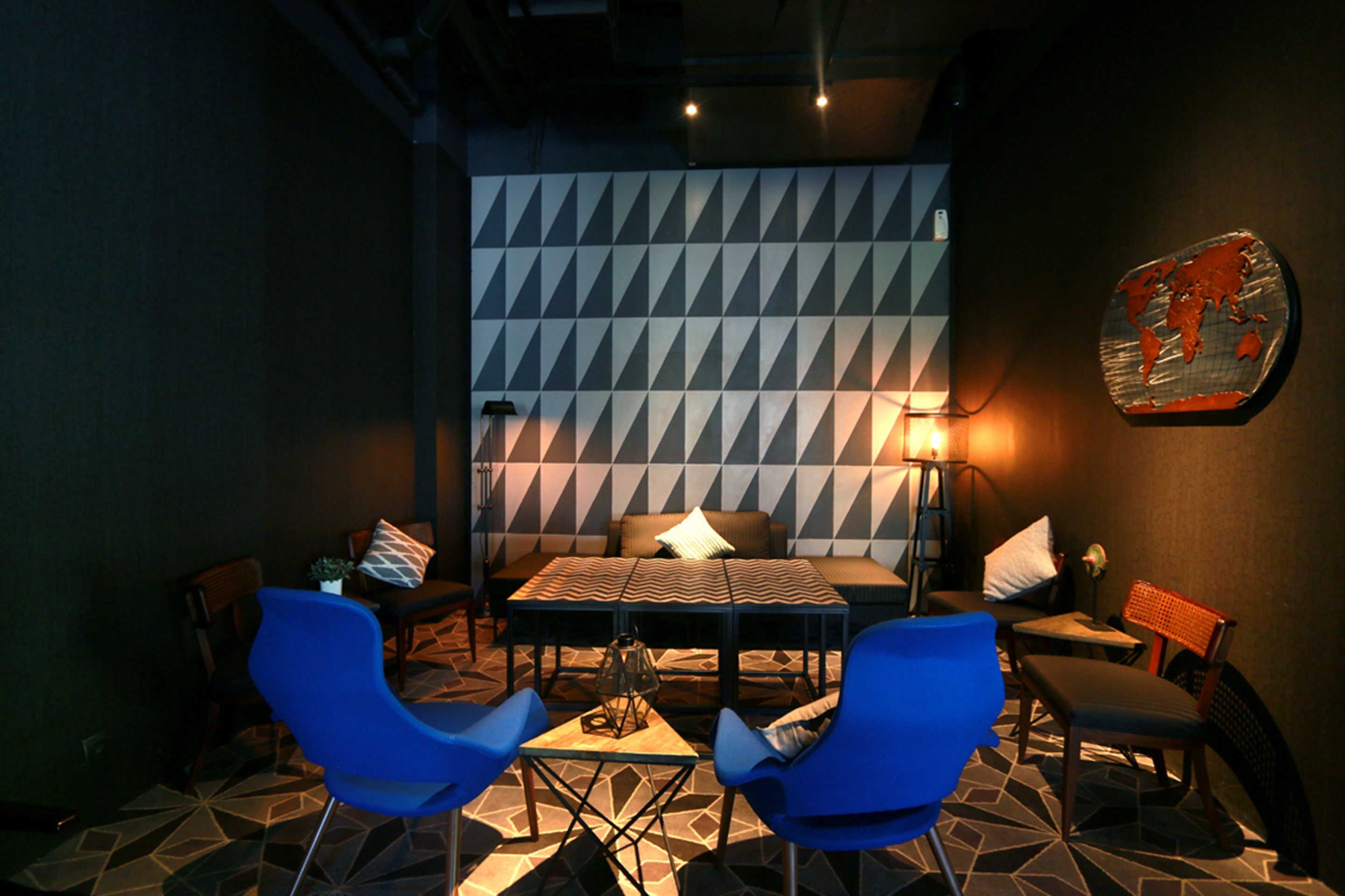 Un interior moderno con un revestimiento mural de estampado geométrico, una mesa central con sillas y una decoración con mapa del mundo.