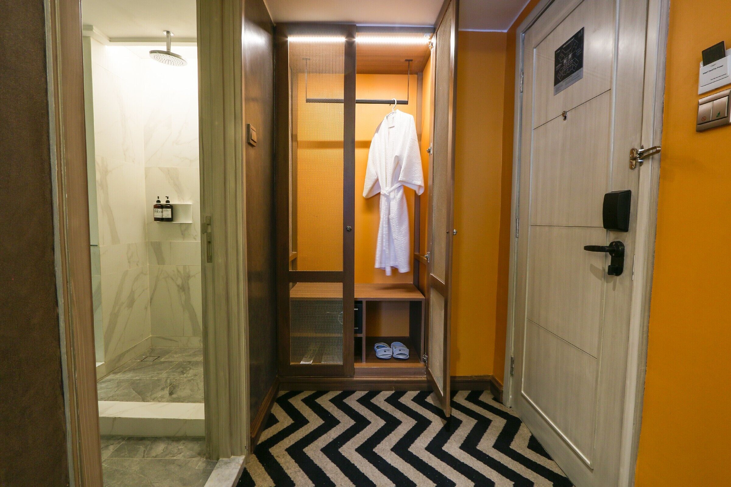 A hotel bathroom with a shower, a robe hanging, and a shoe rack.
