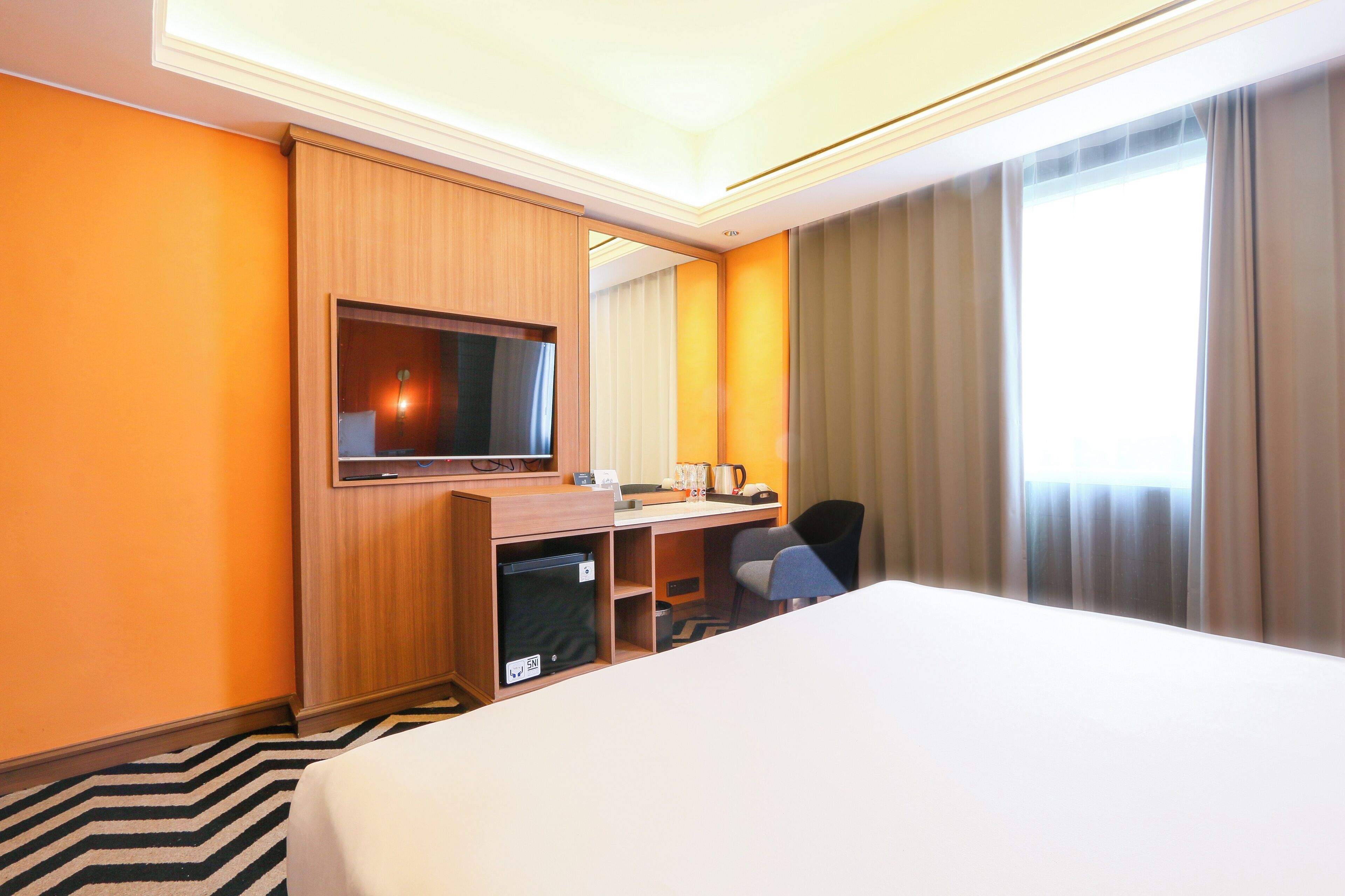 A hotel room with a bed, desk, chair, television, and a window with curtains.