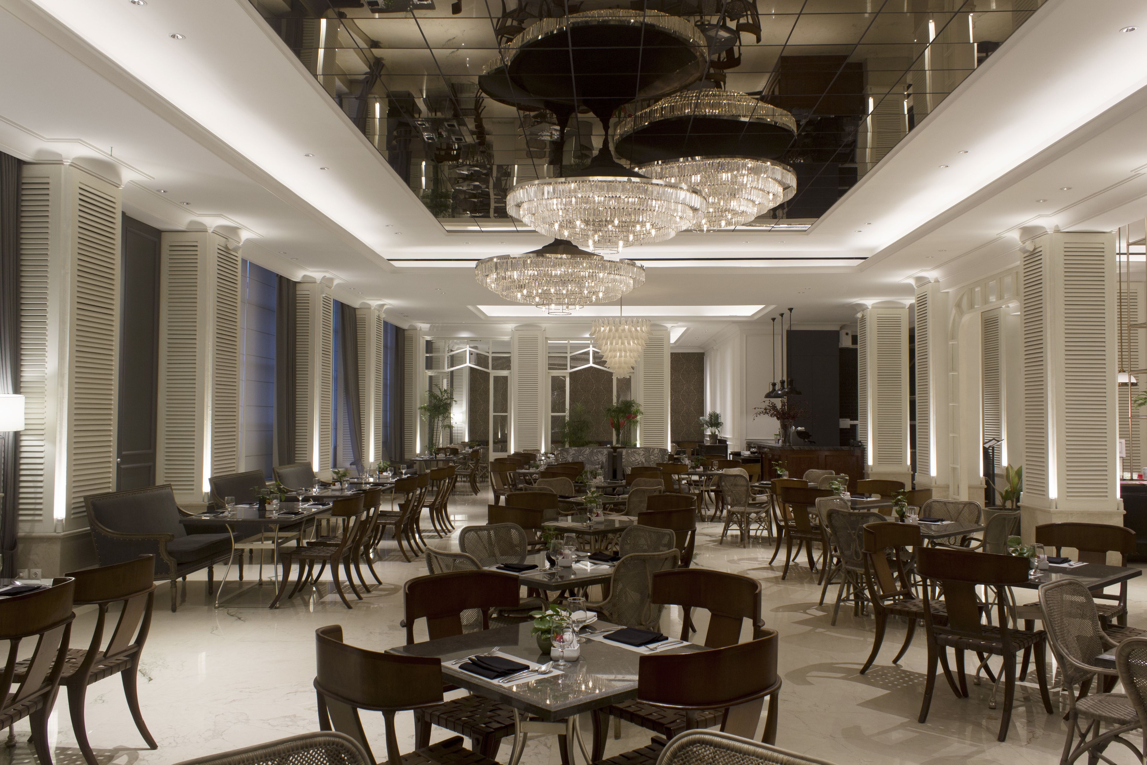 A spacious dining area with multiple tables and chairs, elegant chandeliers, and a modern interior design.