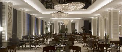 A spacious dining area with multiple tables and chairs, elegant chandeliers, and a modern interior design.