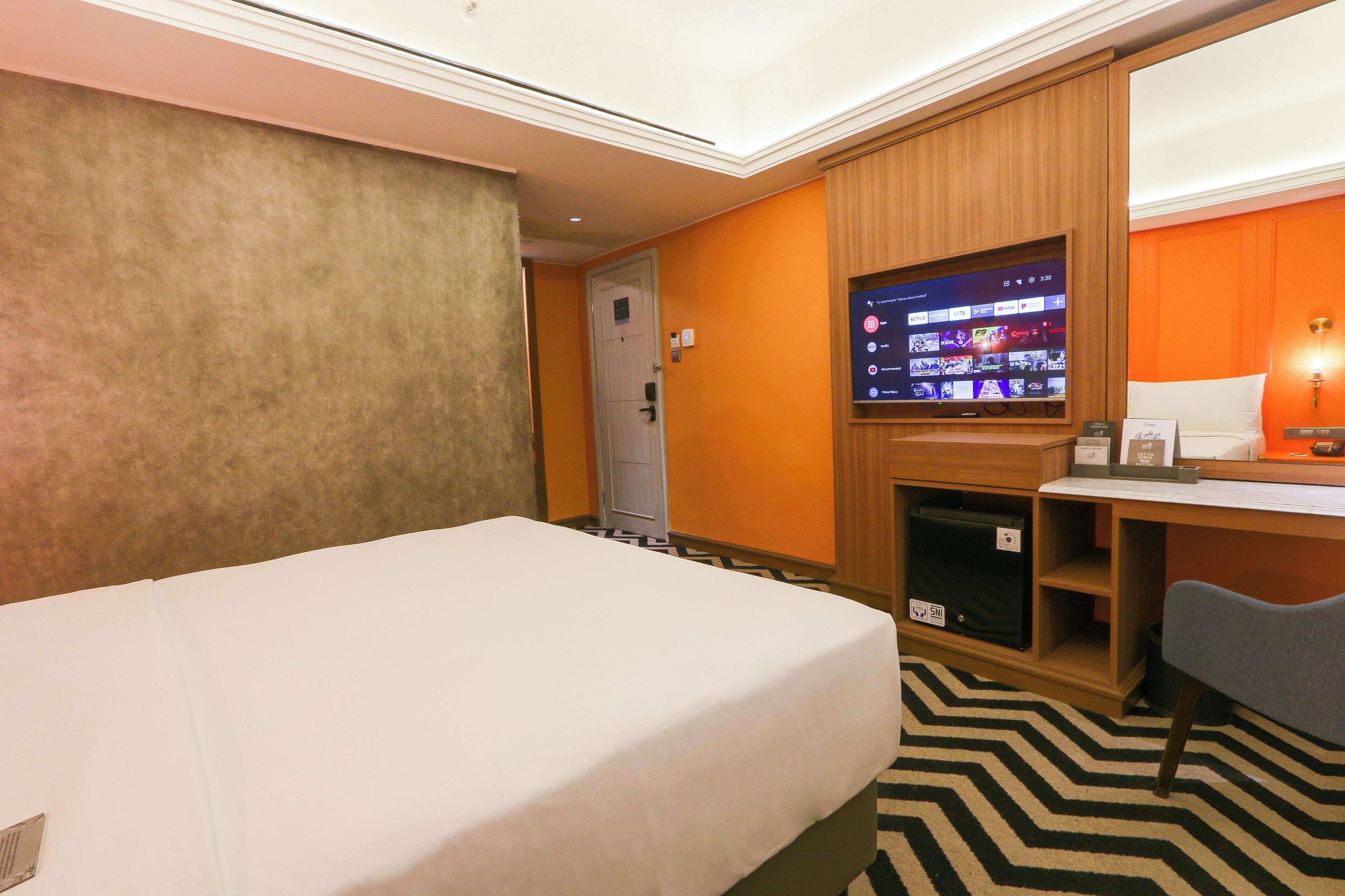 A hotel room with a bed, a desk, a television, and a door.