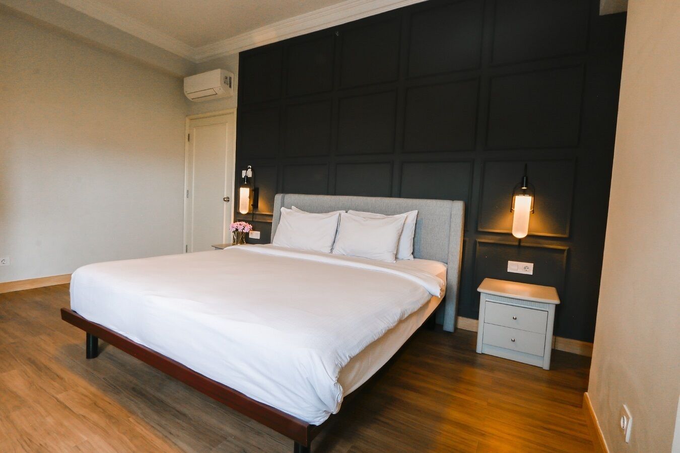 Una habitación de hotel con una cama grande, mesitas de noche, aire acondicionado de pared y una pared de acento oscura.