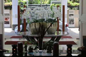 A reception area with a glass partition, a table with a vase of white orchids, and a car parked outside. - Java Paragon Hotel and Residences (Surabaya)