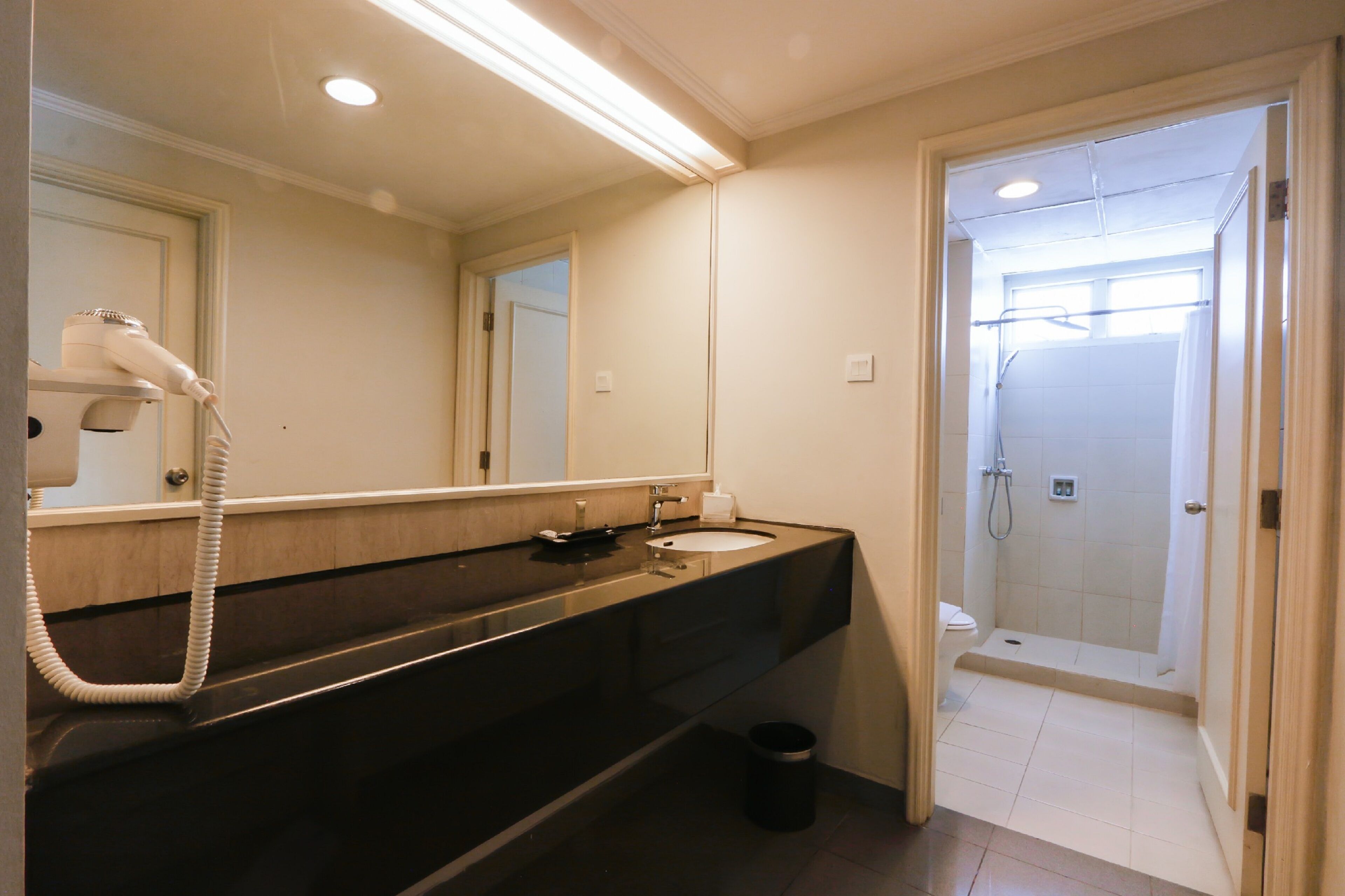 Une salle de bain équipée d’un sèche-cheveux, d’un lavabo, d’un miroir et d’un espace douche.