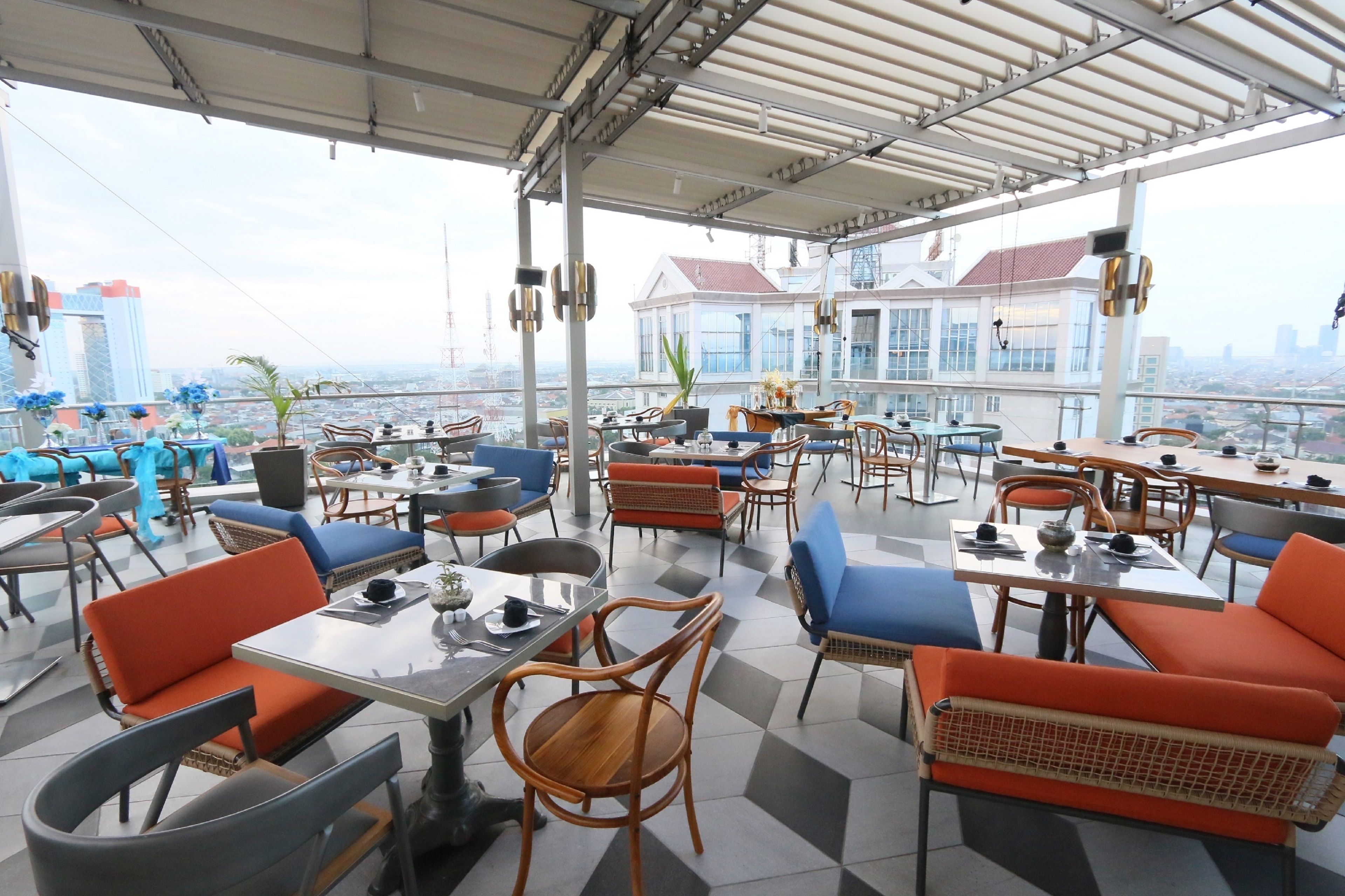 Un restaurante en la azotea con mesas y sillas al aire libre, con vistas a un paisaje urbano.